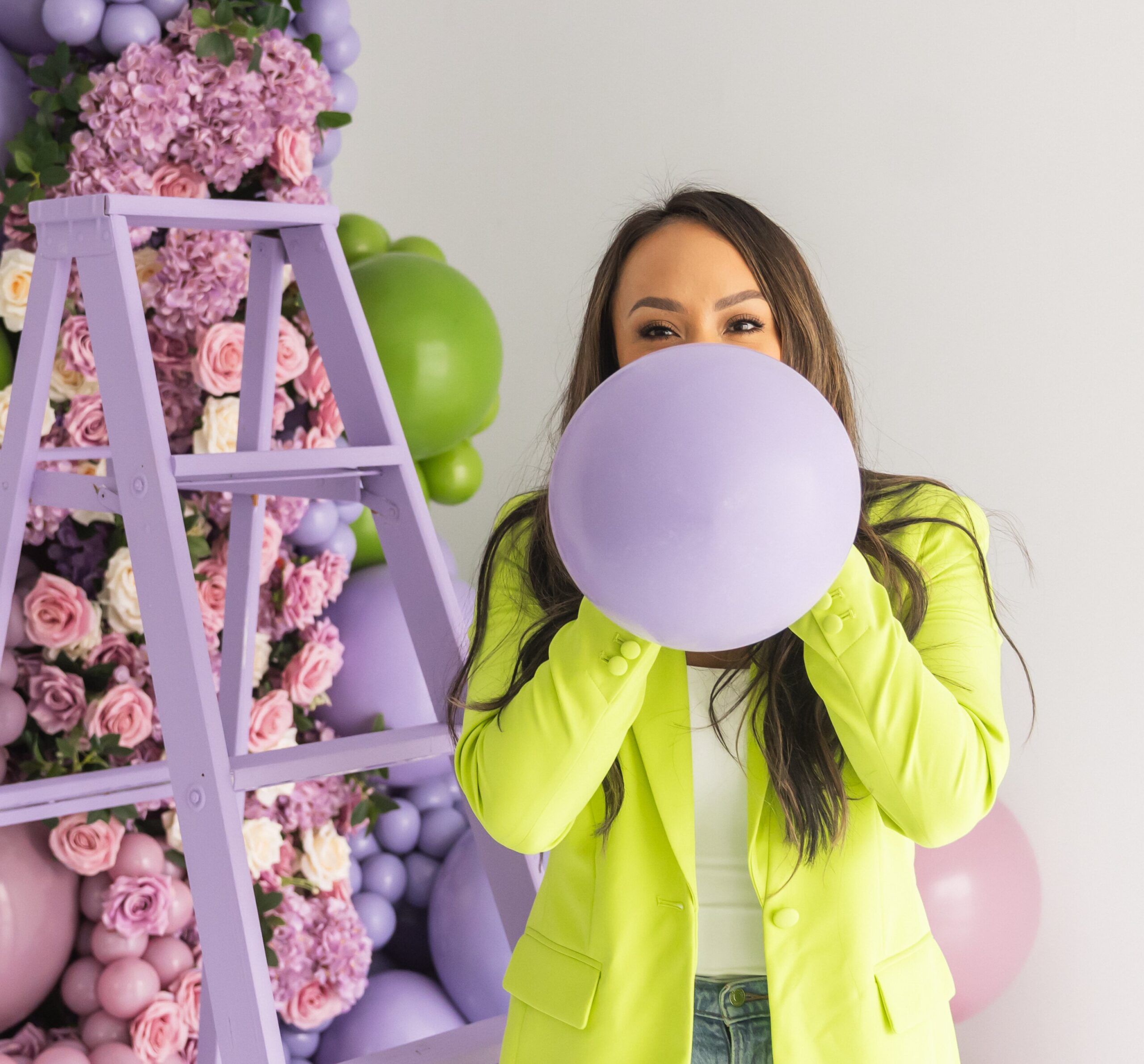 balloon artist holding a purple balloon in front of a floral and balloon arch