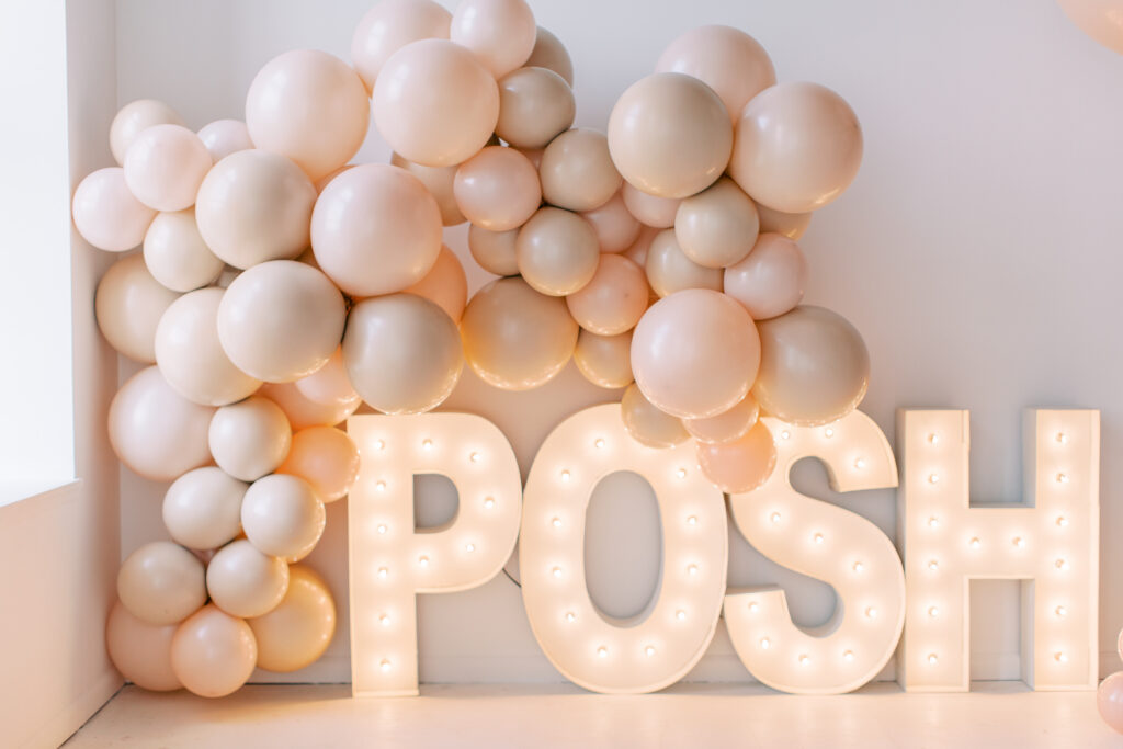Blush balloon garland framing a glowing POSH marquee sign