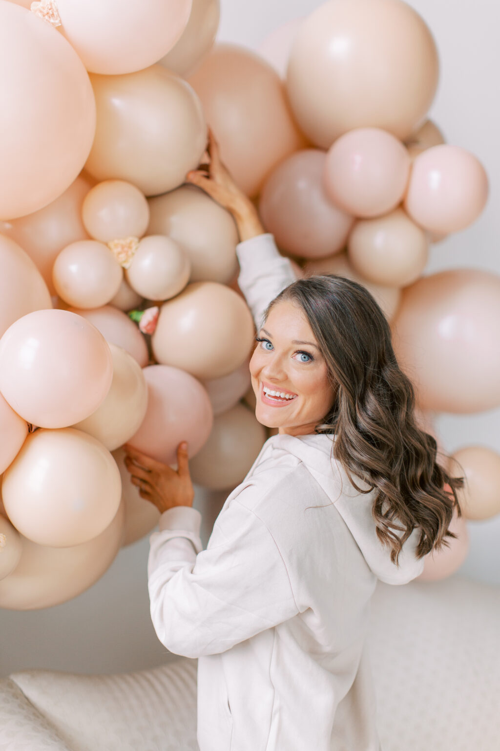 The Posh Balloon owner smiling over her shoulder beside a blush balloon wall