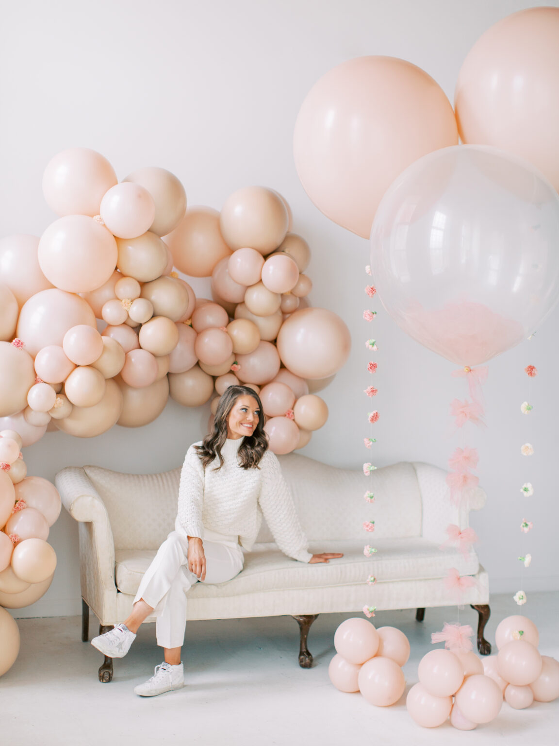 The Posh Balloon owner on a cream settee in front of a blush balloon wall