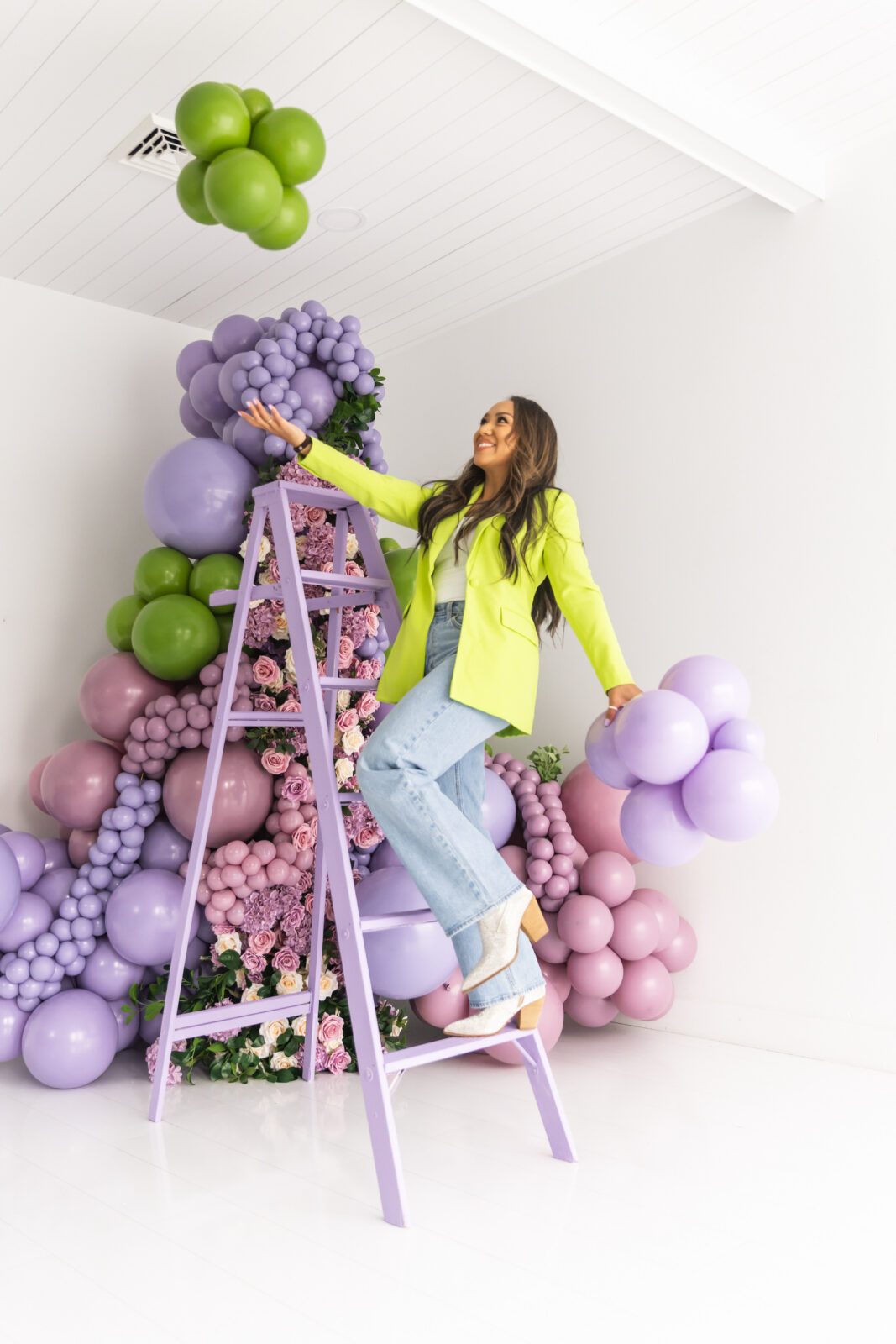 Subtle Flex Designs owner reaching up to a lavender and pink balloon install on a lavender ladder