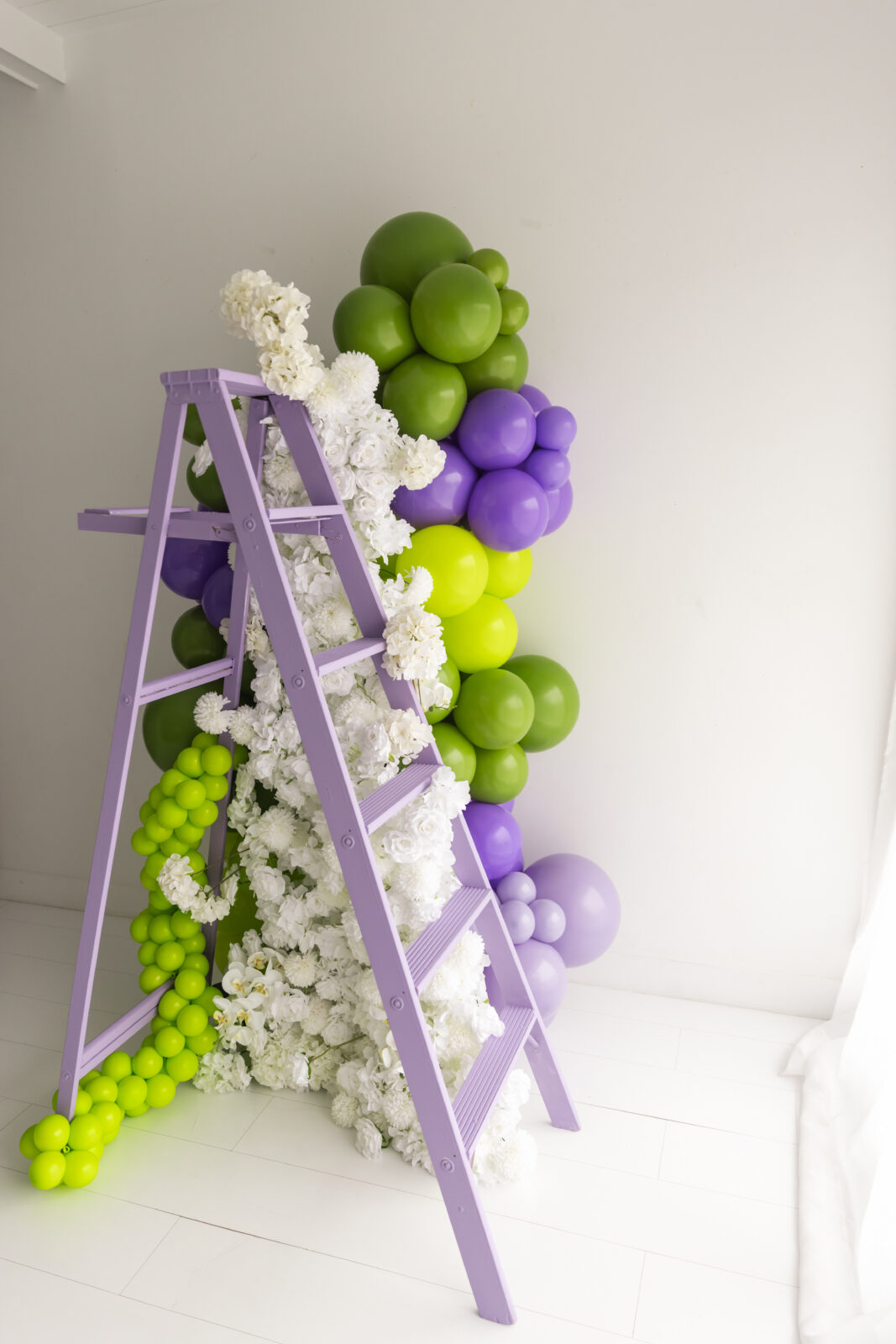 Lavender ladder styled with a green and purple balloon garland and white florals by Subtle Flex Designs