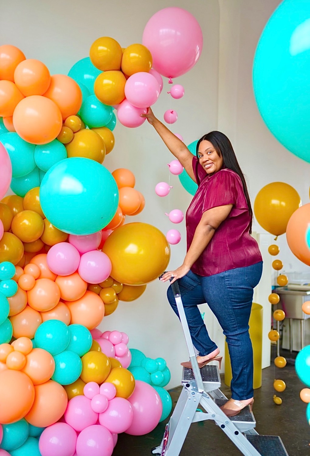 Balloon artist on a ladder building a pink and teal balloon install for her website portfolio