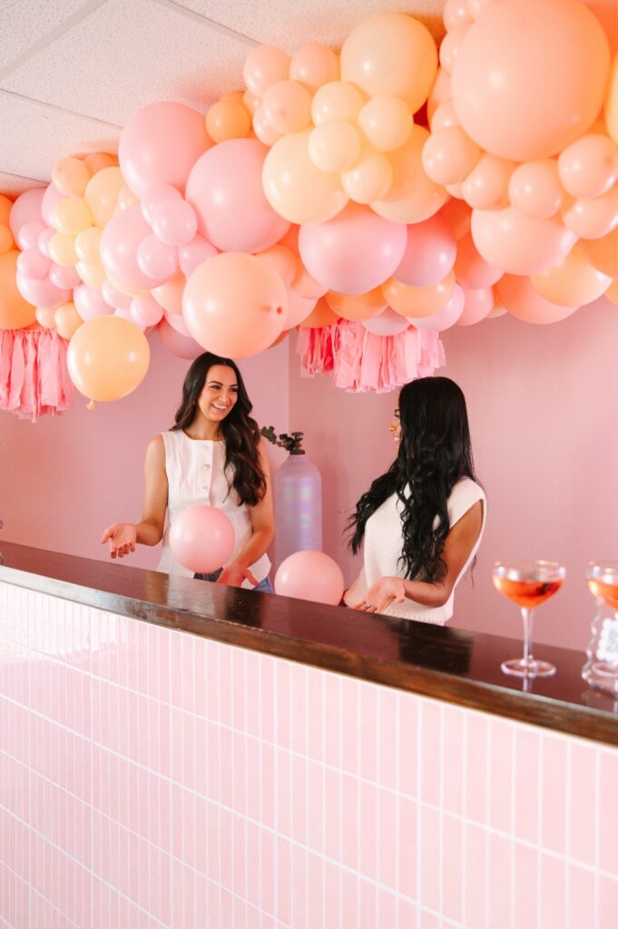 Pop Clink Events owners behind their pink tiled bar under a peach and pink balloon garland in Richmond, VA