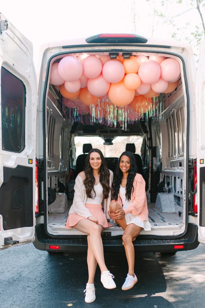 Pop Clink Events owners sitting in their balloon filled delivery van with a pink and peach ceiling install